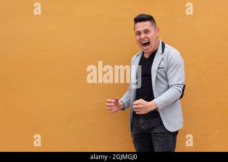 Mann gegen gelbe Wand. Der Mann, der einen Sieg errungen hat, ruft mit seiner Körpersprache. Stockfoto