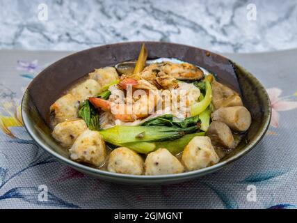 Dünne Reisnudelsuppe mit Muscheln, Garnelen, Fleischbällchen, Pilzen und Gemüse, serviert in einer Keramikschale. Asiatische Küche, selektiver Fokus. Stockfoto