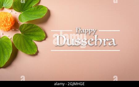 Frohes Dussehra. Gelbe Blüten, grünes Blatt und Reis auf orangefarbenem pastellfarbenem Hintergrund. Dussehra Indian Festival Konzept. Stockfoto