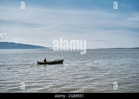 Bursa. Golyazi (Apolyont). Türkei. Ein Mann auf dem kleinen Boot im See von Uluabat während eines sonnigen Tages mit bewölktem Himmel und riesigem Berghintergrund. Stockfoto