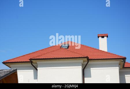 Nahaufnahme eines Dachfenster mit rotem Metalldach, Dachrinne, Kamin und Überwachungskameras. Stockfoto