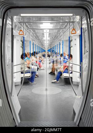 Pendler im U-Bahn-Wagen. Die Menschen sitzen in einer modernen, hellen U-Bahn-Kutsche. Symmetrie im Rahmen. Moskau, RUSSLAND, 21.08.2021. Stockfoto