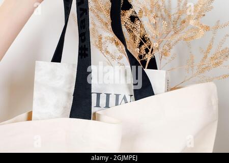 Nachbau der Frauenhand, die wiederverwendbare Öko-Tasche aus weißer Baumwolle mit schwarzen Griffen und trockenen Blumen hält und in der Zeitung auf weiß isoliert liegt Stockfoto