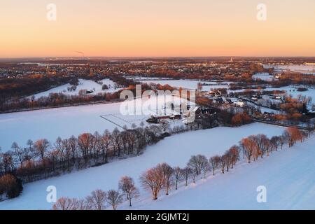 Drohnenansicht von Landschaft und Feldern in Deutschland, die während des Sonnenuntergangs mit Schnee bedeckt sind Stockfoto