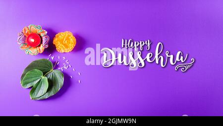 Frohes Dussehra. Gelbe Blüten, grünes Blatt und Reis auf violettem pastellfarbenem Hintergrund. Dussehra Indian Festival Konzept. Stockfoto