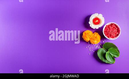 Frohes Dussehra. Gelbe Blüten, grünes Blatt und Reis auf violettem pastellfarbenem Hintergrund. Dussehra Indian Festival Konzept. Stockfoto