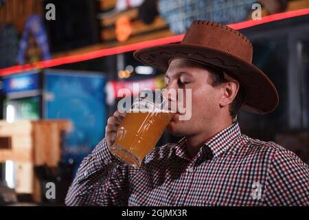 Nahaufnahme eines Mannes mit Cowboyhut, der im Pub Bier aus dem Becher schlürft Stockfoto