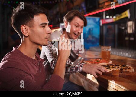 Der junge Mann nippte Bier, nachdem er mit seinem Freund an der Bar Pizza gegessen hatte Stockfoto