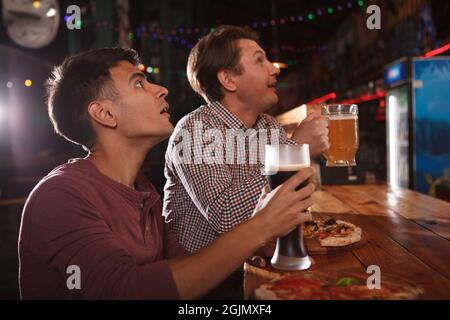 Zwei männliche Freunde, die Bier trinken, während sie sich das Spiel im Bierkneipe ansehen Stockfoto