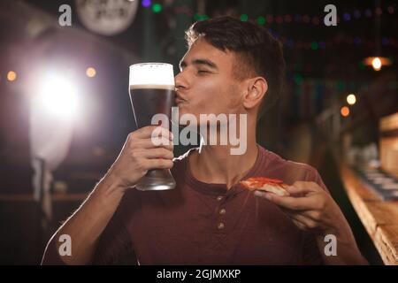 Junger Mann küsst ein Glas Bier und hält Pizza in der Kneipe Stockfoto