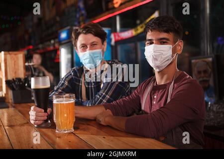 Zwei Barkeeper mit medizinischen Gesichtsmasken arbeiten während einer Coronavirus-Pandemie sicher in ihrem Pub Stockfoto