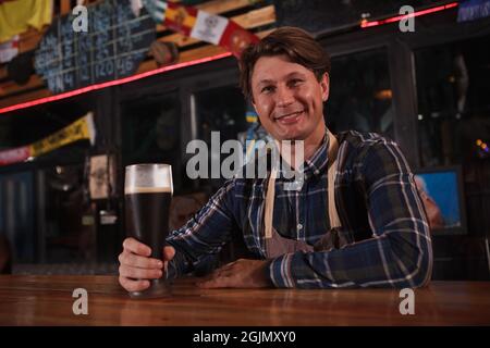 Glücklicher reifer Barkeeper, der lächelte zur Kamera und arbeitete in seinem Bierkneipe Stockfoto