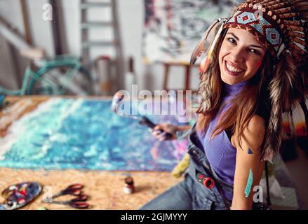 Nahaufnahme einer jungen Künstlerin mit einer Kriegshaube, während sie in angenehmer Atmosphäre im Studio für ein Foto posiert. Kunst, Malerei, Atelier Stockfoto