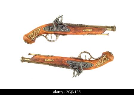 Zwei Nachbauten alter alter, alter Feuerwaffen-Pistolen mit bronzefarbener Intarsien, isoliert auf weißem Hintergrund. Speicherplatz kopieren. Stockfoto