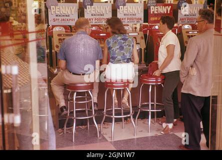 Las Vegas 1959. Anonyme Frau und Mann von hinten an Spielautomaten abgebildet. Eine Maschine, in der Sie eine Münze einwerfen und einen Hebel ziehen, der das Drehen von drei Rollen beginnt. Sobald sie stehen bleiben und die drei dasselbe Symbol zeigen, gewinnen Sie. Kodachrome Dia Original. Credit Roland Palm Ref. 6-2-15 Stockfoto