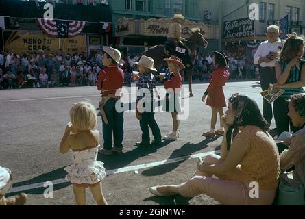 Las Vegas 1959. Eine Parade führt durch die Innenstadt von Las Vegas und die Fremont Street und die Menschen stehen auf den Bürgersteigen und schauen. Im Vordergrund eine Gruppe von Kindern, die alle in Cowboy-Outfits gekleidet sind und die Reiter anfeuern, die auf der Straße vorbeikommen. Kodachrome Dia Original. Kredit Roland Palm. Stockfoto