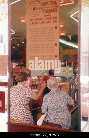 Las Vegas 1959. Anonyme Frauen von hinten an Spielautomaten abgebildet. Eine Maschine, in der Sie eine Münze einwerfen und einen Hebel ziehen, der das Drehen von drei Rollen beginnt. Sobald sie stehen bleiben und die drei dasselbe Symbol zeigen, gewinnen Sie. Kodachrome Dia Original. Credit Roland Palm Ref. 6-2-14 Stockfoto