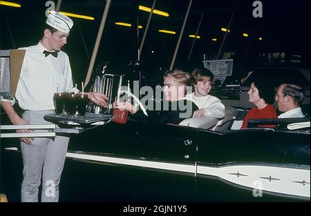 USA in den 1960er Jahren. Zwei junge Paare in einem Cabrio in einem Huddle Drive-in-Restaurant 1964. Ein Kellner erhält die Bezahlung für die alkoholfreien Getränke. Kodachrome Dia Original. Credit Roland Palm Ref. 6-9-17 Stockfoto