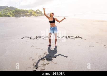 Blonde Frau, die an einem Strand mit Inschriften im Sand steht, um glücklich zu sein. Costa Rica Stockfoto