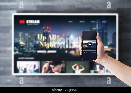 Filmübertragung mit fernseher und Telefon. Mockup der VOD-Serie (Watching on Demand) mit Smart-TV und Mobiltelefon. Mann, der die Videoplayer-App mit Fernbedienung verwendet. Stockfoto