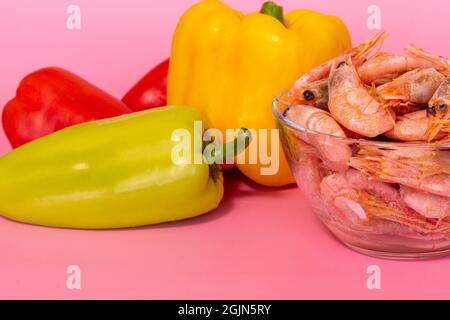 Frisch gefärbte Paprika und gekochte Garnelen auf rosa Hintergrund, gesundes Lebensmittelkonzept Stockfoto