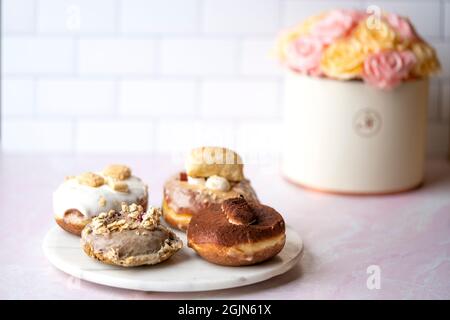 Mehrere Arten von Donuts auf einer Marmorplatte, Blumen im Hintergrund Nahrung Stockfoto