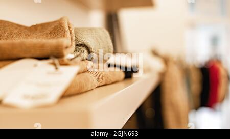 Strickkleider und beige Pullover stehen im Regal. Modische Damenbekleidung. Markenkleidung in einem Showroom. Modegeschäft, Showroom, Einkaufsmöglichkeiten Stockfoto