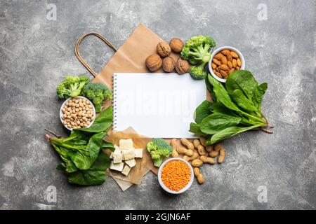 Konzept: Kaufen Sie gesunde, saubere Lebensmittel. Proteinquelle für Vegetarier: Gemüse, Nüsse und Hülsenfrüchte Draufsicht auf einem konkreten Hintergrund mit einem Papierbeutel Stockfoto