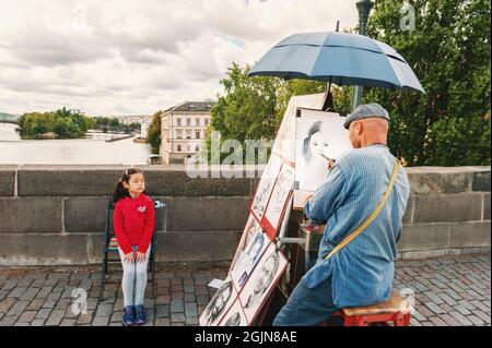 PRAG, TSCHECHISCHE REPUBLIK - 13. August 2017: Ein Künstler malt ein Porträt eines Mädchens auf der geschäftigen Karlsbrücke in Prag Stockfoto