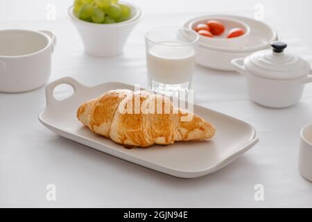 Frühstück mit Croissants, frischen Trauben, Eiern, Tomaten, Milch, Butter und Orangenmarmelade Stockfoto