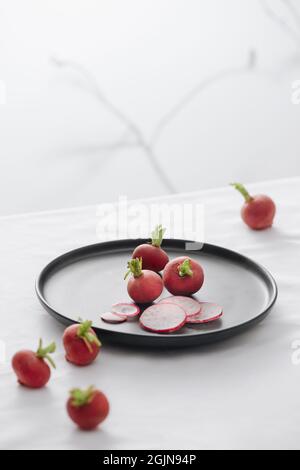 Frische rote Radieschen mit Stiel und Wurzeln in einer schwarzen Schale auf dem Tisch Stockfoto