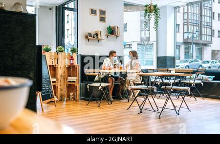 Pärchen mit Gesichtsmaske, die in einem Café Getränke trinken Stockfoto