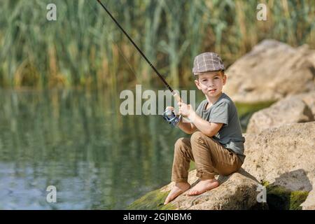 Kleiner Junge sitzt auf Stein und fischt Stockfoto