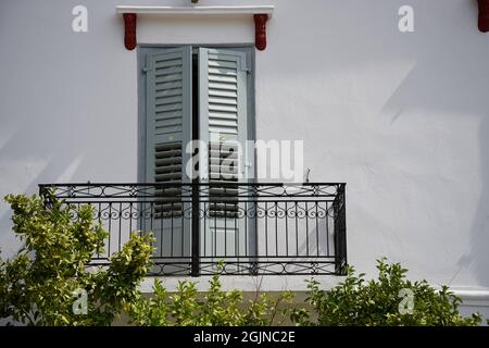 Traditionelle ländliche Hausfassade mit hölzernen Fensterläden und einem Balkon mit handgefertigtem Eisengeländer an einer weiß getünchten Wand in Galaxidi Phocis Griechenland Stockfoto