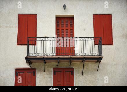 Ländliche Hausfassade mit einer weiß getünchten Wand, karmesinroter Holztür und Fensterläden und einem Balkon mit einem handgefertigten geschmiedeten Eisengeländer in Galaxidi GR. Stockfoto