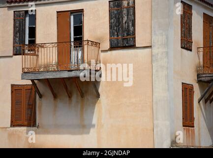 Traditionelle ländliche Hausfassade mit einer venezianischen Stuckwand, hölzernen Fensterläden und einem Balkon mit einem handgefertigten Eisengeländer in Galaxidi, Griechenland. Stockfoto