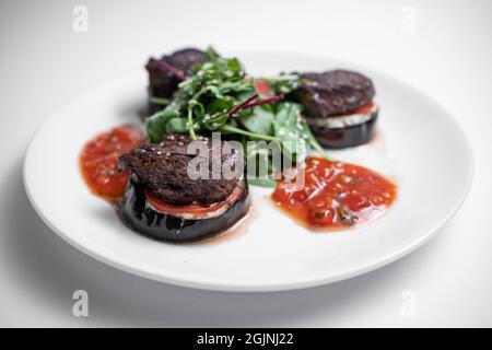 Nahaufnahme von Fleischrindmedaillon auf Tomate und gegrillter Aubergine mit Salsa-Sauce Stockfoto