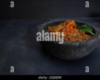 Bilder von „sambal“, einem indonesischen würzigen Essen auf einer Steinschale. Nehmen Sie auf schwarzem Hintergrund auf Stockfoto