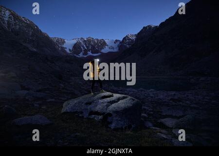 Tourist Mann in gelber Jacke mit Stirnlampe in den Schneebergen unter Nachthimmel mit Sternen. Stockfoto