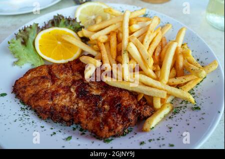 Wiener Schnitzel serviert mit französischer Bratkartoffel und frischem Salat aus nächster Nähe Stockfoto