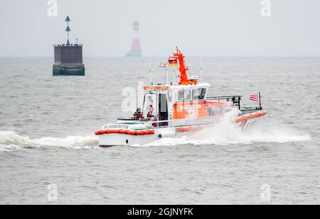 Wilhelmshaven, Deutschland. September 2021. Der Rettungskreuzer 'Peter Habig' der Deutschen Seesuche und Rettungsdienste (DGzRS) ist bei bewölktem Wetter auf der Jade-Bucht unterwegs. Im Hintergrund ist der historische Leuchtturm Arngast zu sehen. Quelle: Hauke-Christian Dittrich/dpa/Alamy Live News Stockfoto