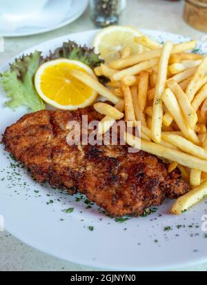 Wiener Schnitzel serviert mit französischer Bratkartoffel und frischem Salat aus nächster Nähe Stockfoto