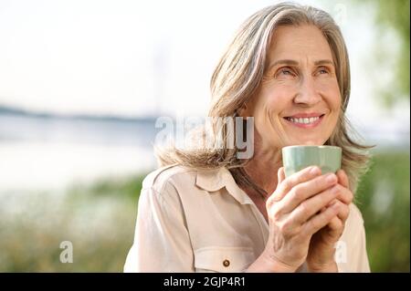 Optimistische lächelnde Frau mit Kaffee im Freien Stockfoto