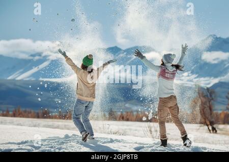 Zwei glückliche junge Mädchen haben Spaß und werfen Schnee in die Berge. Konzept für Winterferien Stockfoto