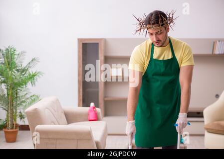 Junger männlicher Auftragnehmer, der auf dem Kopf einen stacheligen Kranz trägt und Hausarbeit leistet Stockfoto