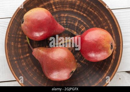 Drei rote Birnen in einer Keramikplatte auf einem Holztisch, Nahaufnahme, Draufsicht. Stockfoto