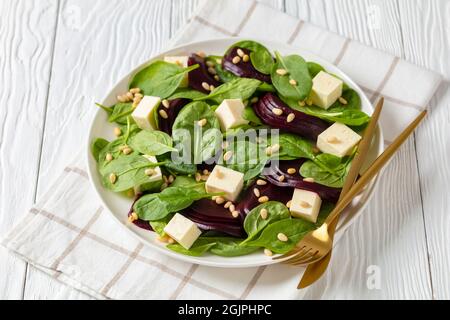 Gerösteter Rübensalat mit gewürfeltem Feta-Käse, Pinienkernen und Spinat auf einem weißen Teller mit goldenem Besteck auf einem Holztisch, kanadische Küche Stockfoto