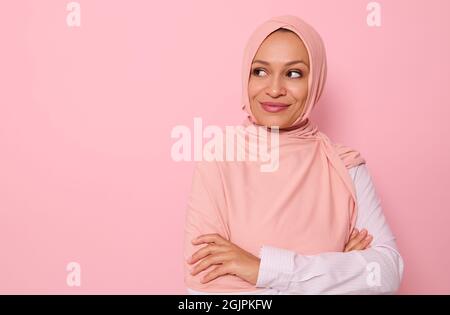 Nahaufnahme Porträt einer arabischen Muslimin mittleren Alters wunderschöne hübsche Frau mit verdecktem Kopf in Hijab, die geheimnisvoll auf der Seite auf einem rosa Hintergrund schaut Stockfoto
