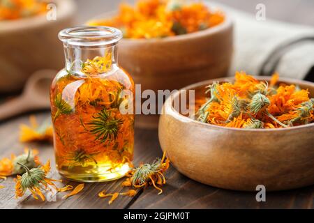 Flasche ätherisches Calendula-Öl, Infusion oder Serum, Holzschale und Mörser aus getrockneten gesunden Ringelblumen. Alternative Medizin. Stockfoto