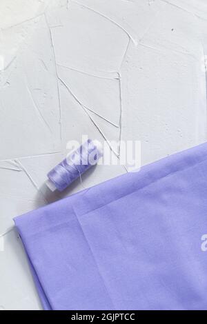 Garn und Baumwollstoff in lila Farbe vor grauem Hintergrund, Slow Fashion und Heimnähkonzept Stockfoto